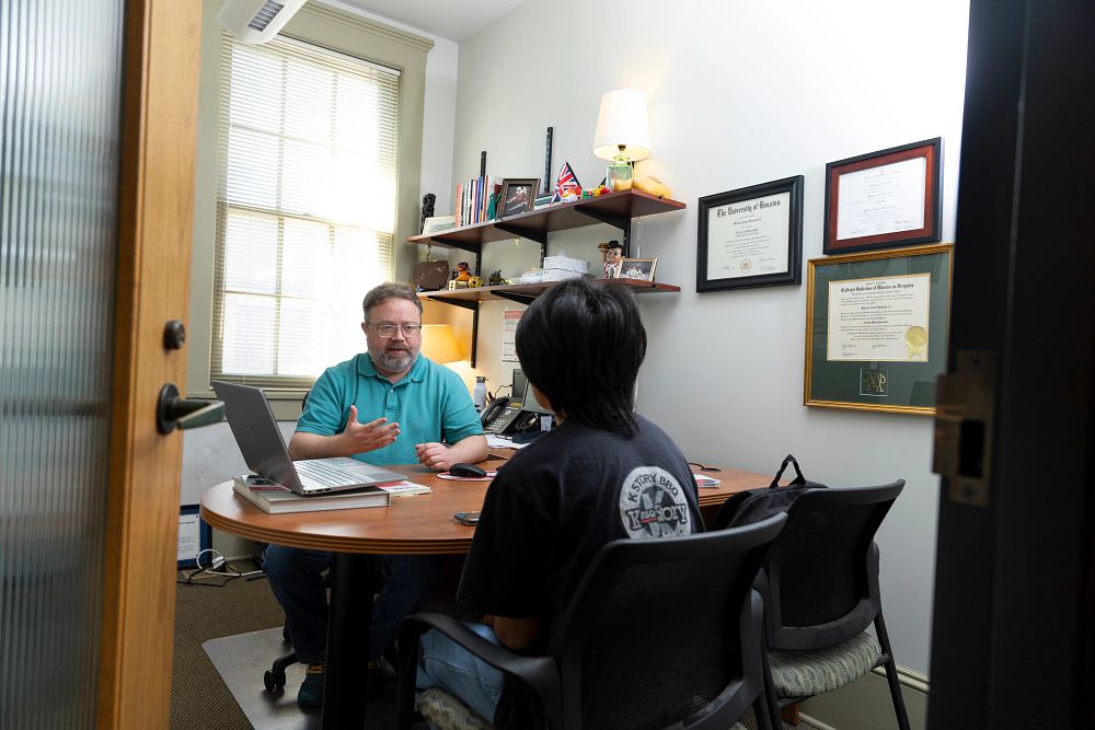 A student talks with an older man at a desk.