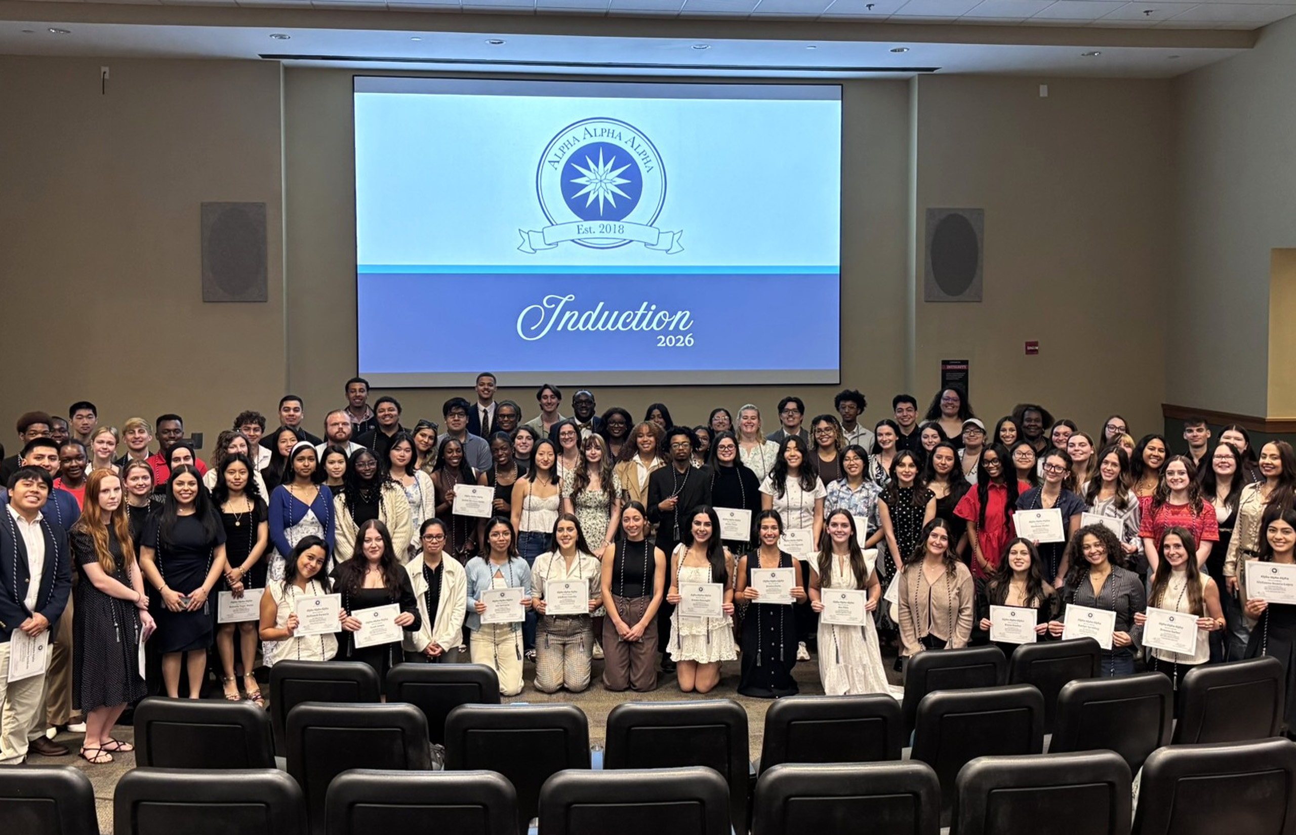 A very large group of first-generation students hold up their diplomas for a photo at the honors induction.