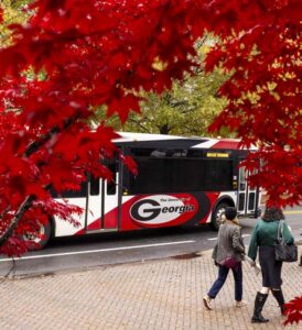 Students walk by a UGA bus with fall foliage overhead