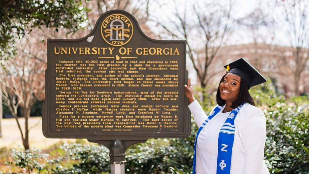 A student standing by a UGA sign