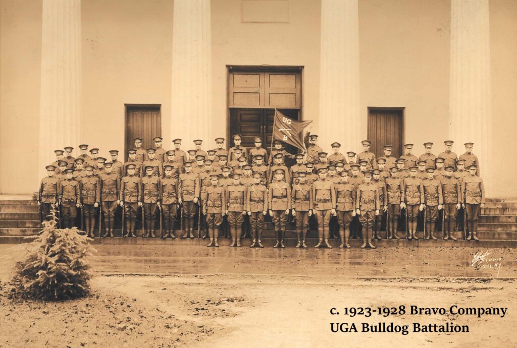 Black and white image of the circa 1923-1928 Bravo Company UGA Bulldog Battalion posing for a formation photo on steps in front of a white building with columns. 